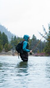 Woman fly fishing in the rain while wading in a river.
